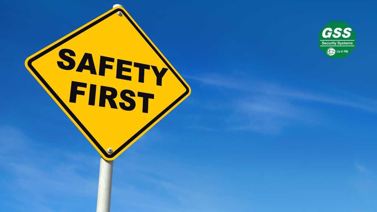 A yellow road sign with bold black text reading "SAFETY FIRST" stands against a bright blue sky with wispy clouds. The "GSS Security Systems" logo is positioned in the upper right corner.
