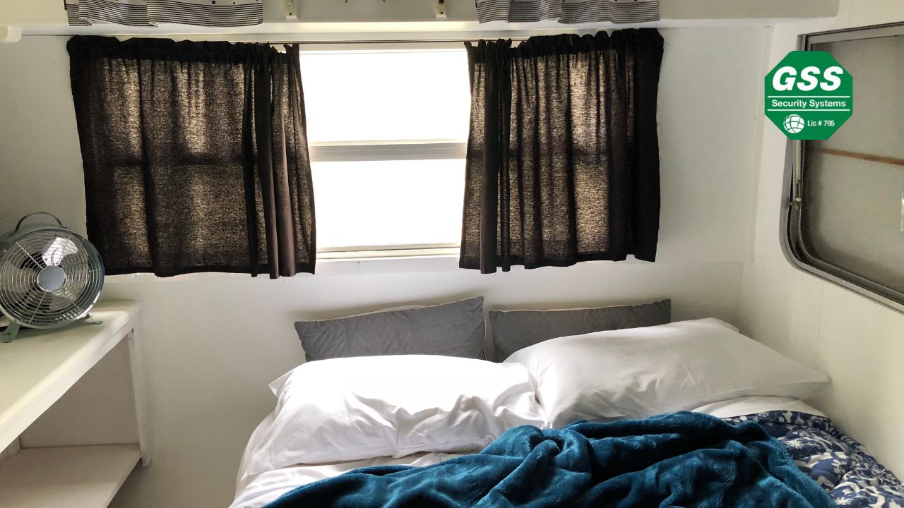 A cozy and organized small bedroom with a neatly made bed, dark curtains, and a fan on a shelf, showcasing efficient use of limited space.
