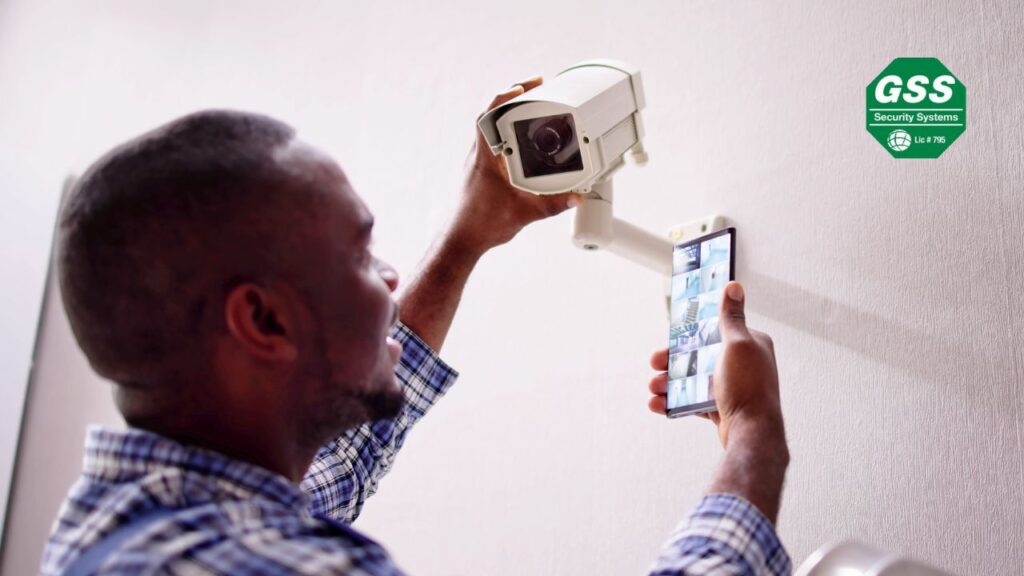 A man installing a security camera on a wall while monitoring live footage on his smartphone, ensuring proper alignment and functionality.